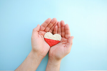 Flag of Poland. Heart shape of white and red plasticine modeling clay in male hands on blue background. Polish flag concept, love. Top view, closeup, copy space.