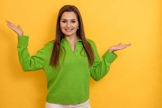 Portrait Of A Cheerful Young Woman In A Green Jumper On A Yellow Background With Her Hands Up