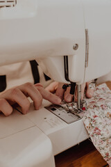 Close up of sewing machine. Crop view of hands of female tailor sewing on machine. Soft focus.