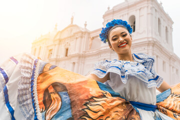 Nicaraguan folklore dancer smiling and looking at the camera outside the cathedral church in the central park of the city of Leon. The woman wears the typical dress of Central America  - obrazy, fototapety, plakaty