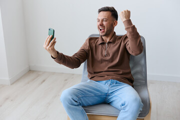 Yeah, cool offer. Celebrating lottery win overjoyed happy young tanned man raise fist up hold phone...