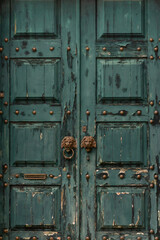 Old wooden door with peeling green paint, metal rivets and lion head handles