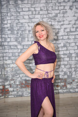 A beautiful blonde dancer in an oriental outfit in the studio against a brick wall