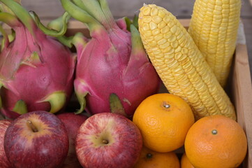 Red apples, Yuzu oranges, corn, dragon fruit arranged in wooden boxes. Red fruits and vegetables contain lycopene. Yellow and orange fruits contain carotenoids, vitamin C.
