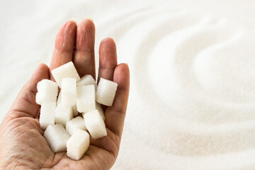 Fototapeta na wymiar White sugar cubes in a handful, on granulated sugar background