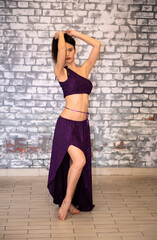 A beautiful model dancer in the studio against a brick wall in an oriental outfit in a gymnastic bend