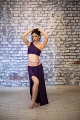 A beautiful model dancer in the studio against a brick wall in an oriental outfit in a model pose