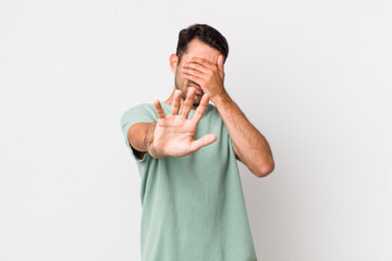 young handsome hicpanic man covering face with hand and putting other hand up front to stop camera,...
