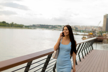 Obraz premium Young woman using a mobile phone while walking on the river promenade