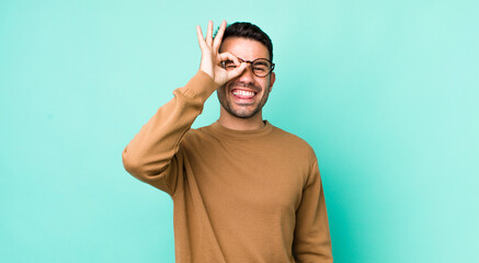 young handsome hicpanic man smiling happily with funny face, joking and looking through peephole,...