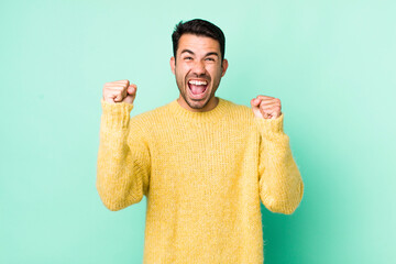 young handsome hicpanic man feeling happy, positive and successful, celebrating victory,...