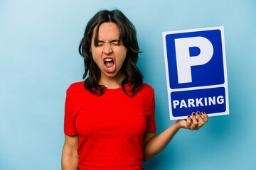 Young hispanic woman holding parking placard isolated on blue background screaming very angry and aggressive.