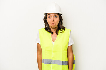 Young laborer hispanic woman isolated on white background shrugs shoulders and open eyes confused.