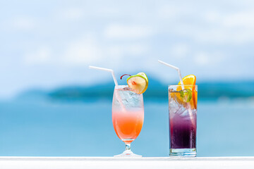 Two cocktail glasses with fruit decorations and a straw on on the railing of a luxury hotel resort with Andaman Sea on background. Fresh alcohol drinks and fruit cocktails. Copy space