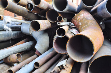 Set of different shaped, rusty pipes stacked on top of each other in a big junkyard. 