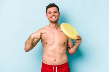 Young caucasian man playing with frisky isolated on blue background person pointing by hand to a...
