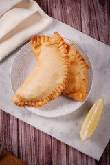 Empanadas traditional argentinian fried food stuffed with meat accompanied with lemon with a background of marble, wood and fabrics.