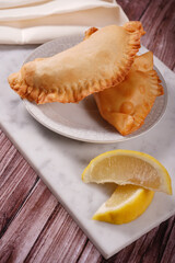 Empanadas traditional argentinian fried food stuffed with meat accompanied with lemon with a background of marble, wood and fabrics.