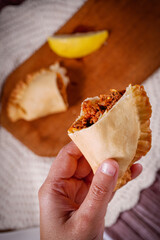 Empanadas traditional argentinian fried meat filled Empanadas with a hand holding a lemon with a background of empanada, lemon, wood and fabrics.