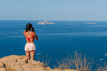 East Asian woman from her back on a cliff in Provence, France, looking at the sea - obrazy, fototapety, plakaty