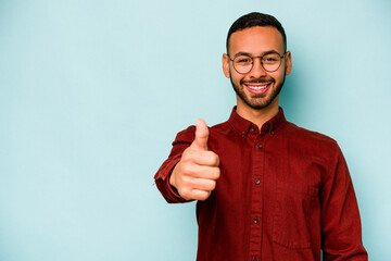 Young hispanic man isolated on blue background smiling and raising thumb up