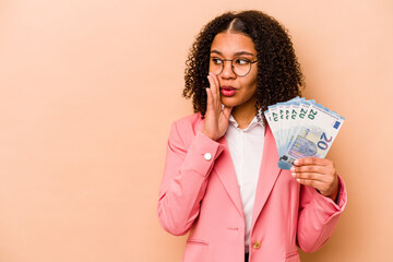 Young African American business woman holding banknotes isolated on beige background is saying a...