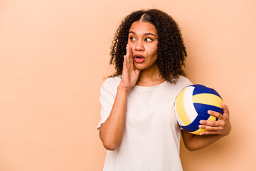 Young African American woman playing volleyball isolated on beige background is saying a secret hot braking news and looking aside