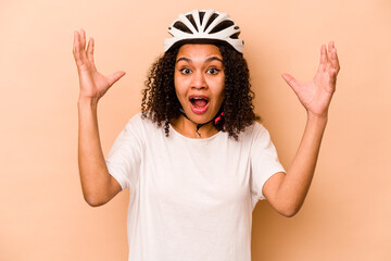 Young hispanic woman wearing a helmet bike isolated on blue background receiving a pleasant surprise, excited and raising hands.