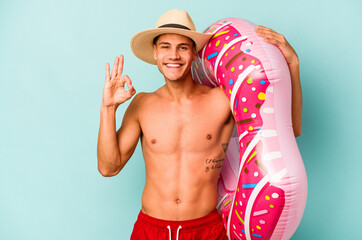 Young caucasian man holding an inflatable donut isolated on blue background cheerful and confident...