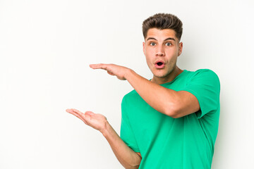 Young caucasian man isolated on white background shocked and amazed holding a copy space between hands.