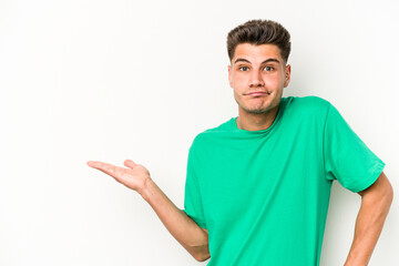 Young caucasian man isolated on white background showing a copy space on a palm and holding another...