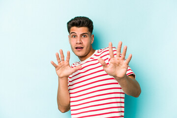Young caucasian man isolated on blue background being shocked due to an imminent danger
