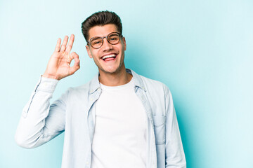 Young caucasian man isolated on blue background cheerful and confident showing ok gesture.