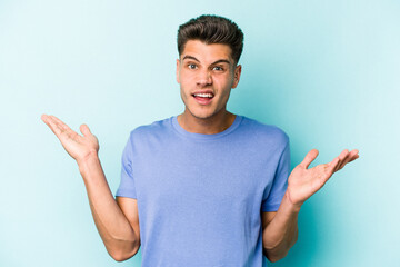 Young caucasian man isolated on blue background confused and doubtful shrugging shoulders to hold a copy space.