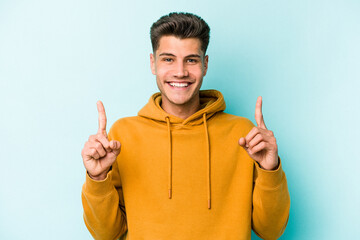 Young caucasian man isolated on blue background indicates with both fore fingers up showing a blank...