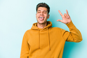 Young caucasian man isolated on blue background showing rock gesture with fingers