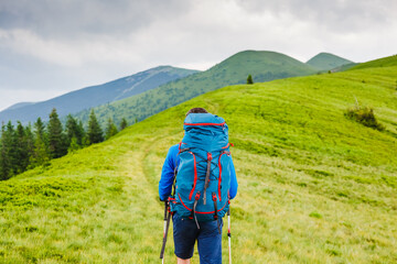 young man with backpack and trekking poles hiking in the mountains