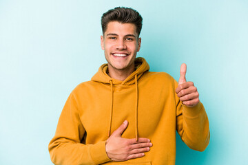 Fototapeta premium Young caucasian man isolated on blue background touches tummy, smiles gently, eating and satisfaction concept.