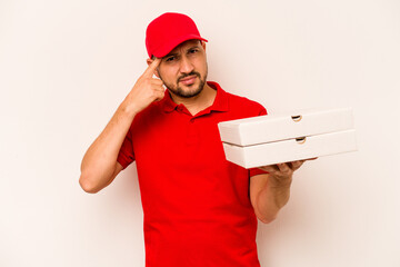 Young delivery man holding pizzas isolated on beige background showing a disappointment gesture with forefinger.