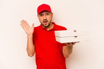 Young delivery man holding pizzas isolated on beige background surprised and shocked.