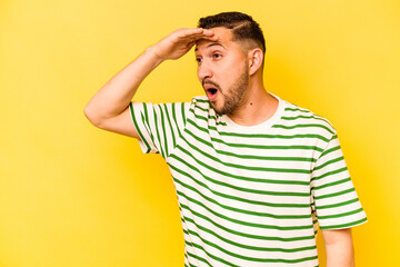 Young hispanic man isolated on yellow background looking far away keeping hand on forehead.