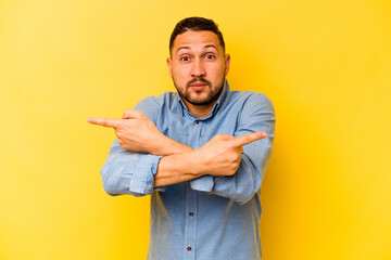 Young hispanic man isolated on yellow background points sideways, is trying to choose between two...