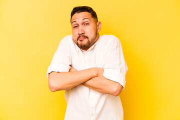 Young hispanic man isolated on yellow background shrugs shoulders and open eyes confused.