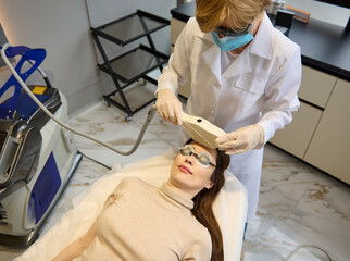Top view of a woman getting facial laser treatment for hair removal, skin smoothing and age and pigments spots treatment on her face in wellness spa clinic