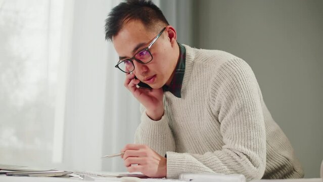 Korean architect designer calling on phone. Professional engineer drawing, interior creator using laptop computer for new house project, blueprint plan, drafting building.