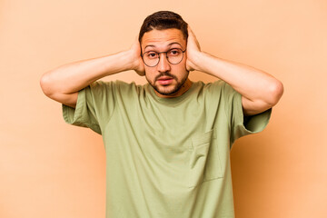 Fototapeta na wymiar Young hispanic man isolated on beige background covering ears with hands trying not to hear too loud sound.