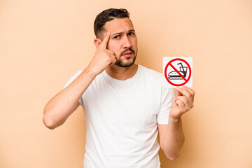 Hispanic caucasian man holding no eating sign isolated on beige background