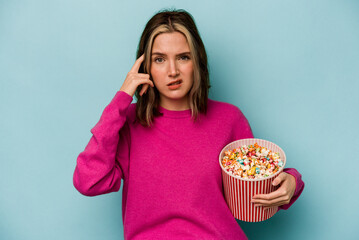 Young caucasian woman holding popcorn isolated on blue background showing a disappointment gesture with forefinger.