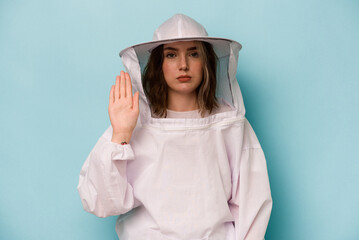 Young caucasian beekeeper woman isolated on blue background standing with outstretched hand showing stop sign, preventing you.