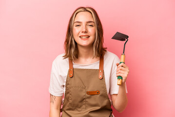 Young gardener woman holding gardening shovel isolated on pink background laughing and having fun.